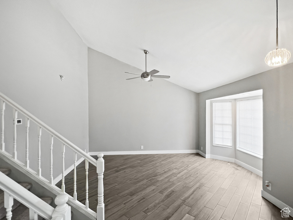 Unfurnished living room with lofted ceiling, wood finished floors, a ceiling fan, stairs, and a chandelier