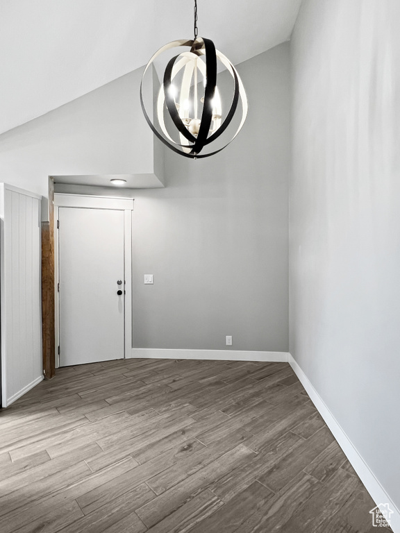 Unfurnished dining area with wood finished floors, a chandelier, and lofted ceiling
