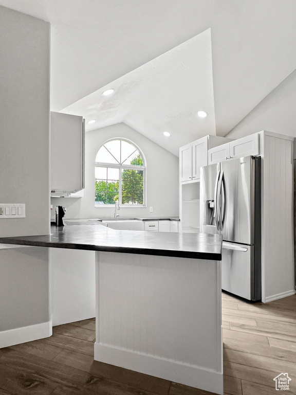 Kitchen featuring stainless steel fridge, lofted ceiling, light wood-style floors, white cabinets, and dark countertops