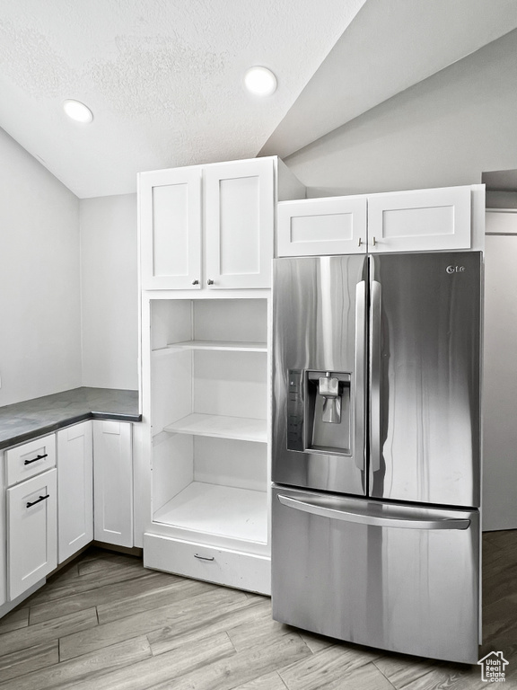 Kitchen with stainless steel fridge with ice dispenser, white cabinets, recessed lighting, light wood-type flooring, and a textured ceiling