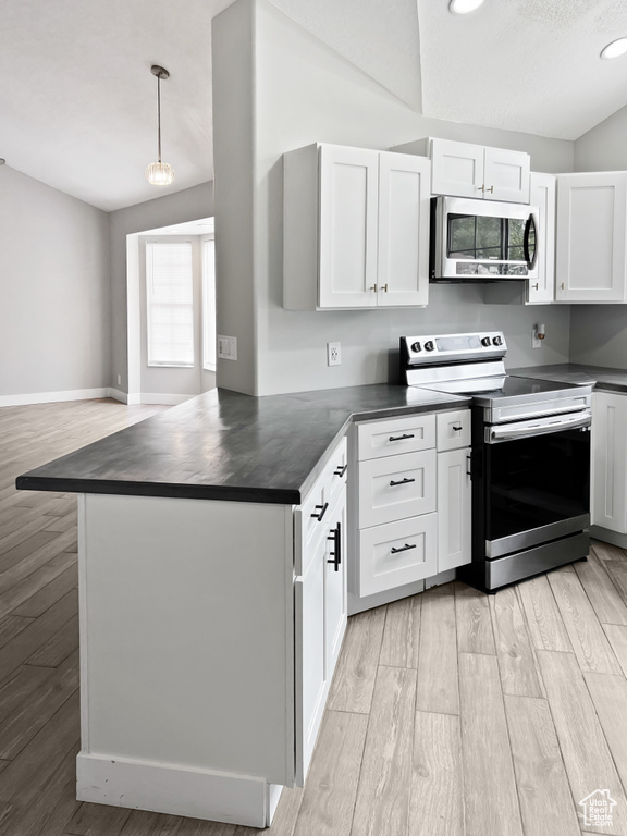 Kitchen featuring stainless steel appliances, dark countertops, light wood-type flooring, white cabinets, and a peninsula