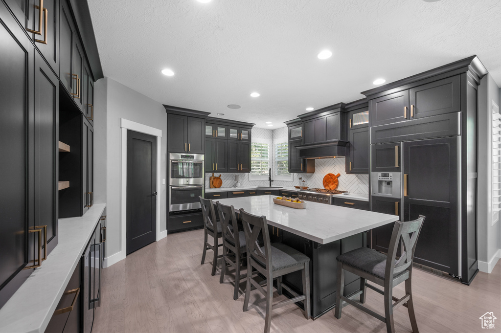 Kitchen featuring paneled fridge, double oven, a breakfast bar, backsplash, and light wood-style flooring