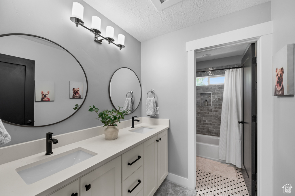 Bathroom with double vanity, shower / bath combo with shower curtain, and a textured ceiling
