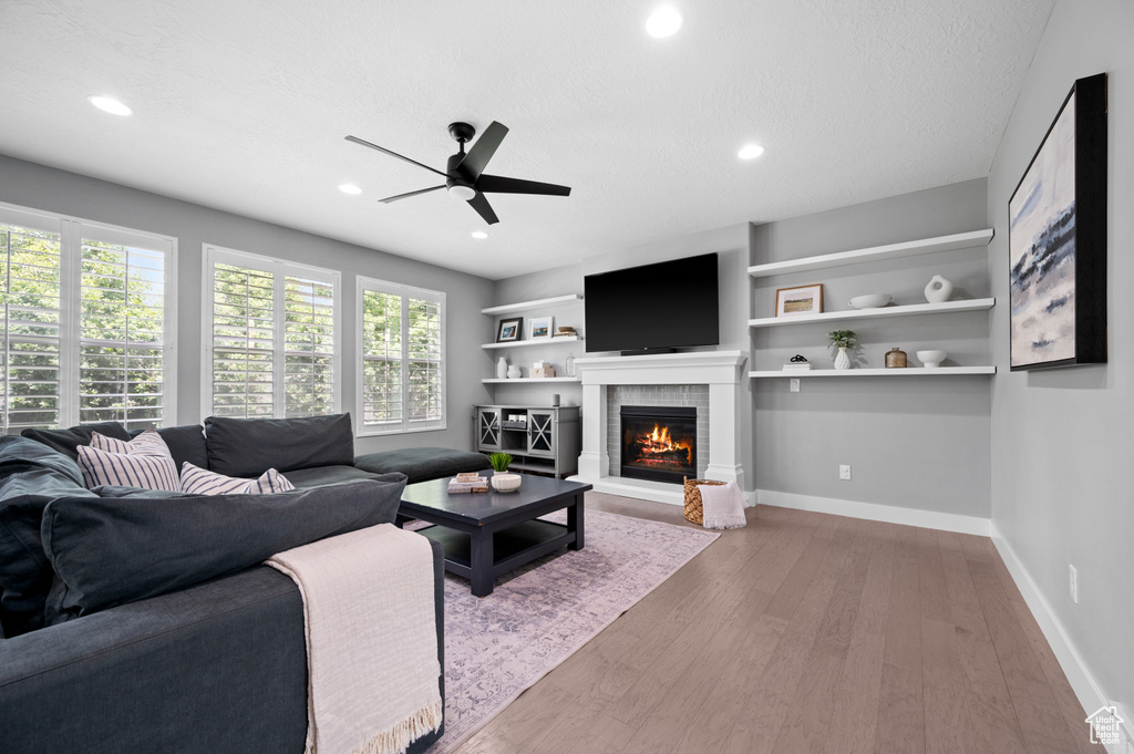 Living area featuring a ceiling fan, wood finished floors, a warm lit fireplace, and recessed lighting