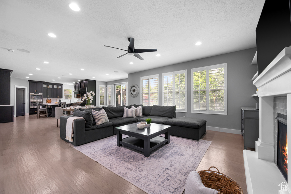 Living room featuring a lit fireplace, ceiling fan, plenty of natural light, recessed lighting, and wood finished floors