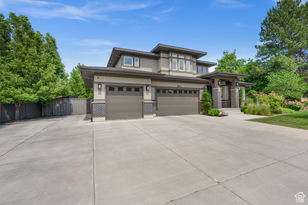 Prairie-style home featuring driveway, a garage, brick siding, and stucco siding