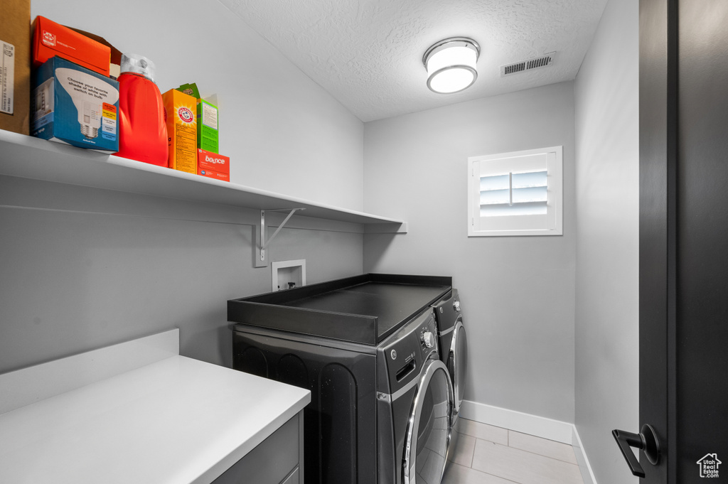 Washroom with washer and dryer, a textured ceiling, and light tile patterned floors
