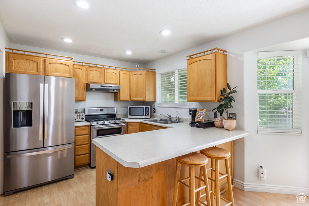 Kitchen with stainless steel appliances, under cabinet range hood, light wood finished floors, light countertops, and recessed lighting