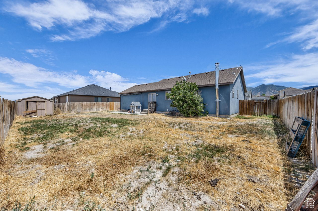 Back of house with a shed, a fenced backyard, stucco siding, and roof with shingles