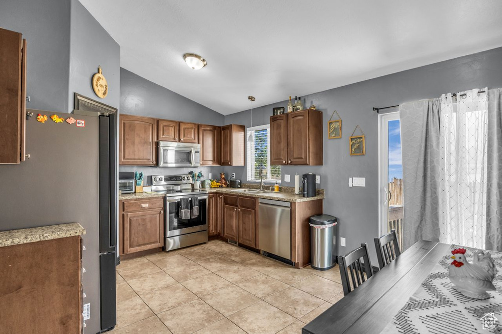 Kitchen with appliances with stainless steel finishes, vaulted ceiling, light tile patterned flooring, light countertops, and brown cabinetry