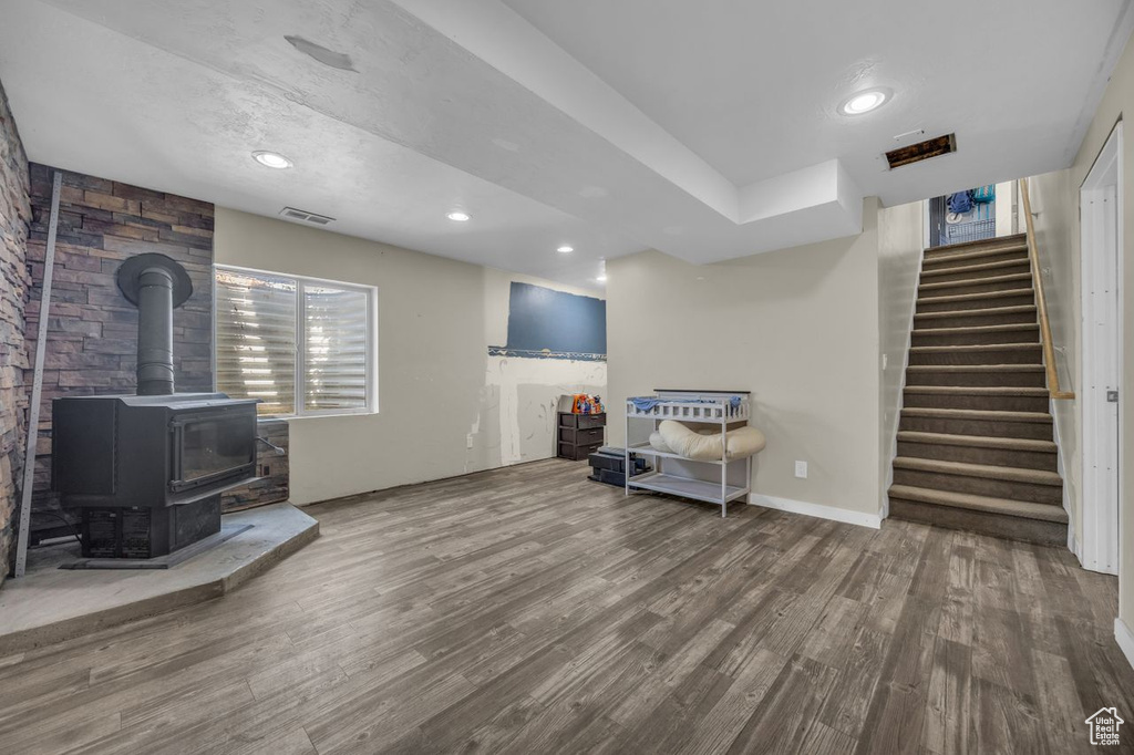 Living room featuring wood finished floors, a wood stove, stairs, and recessed lighting