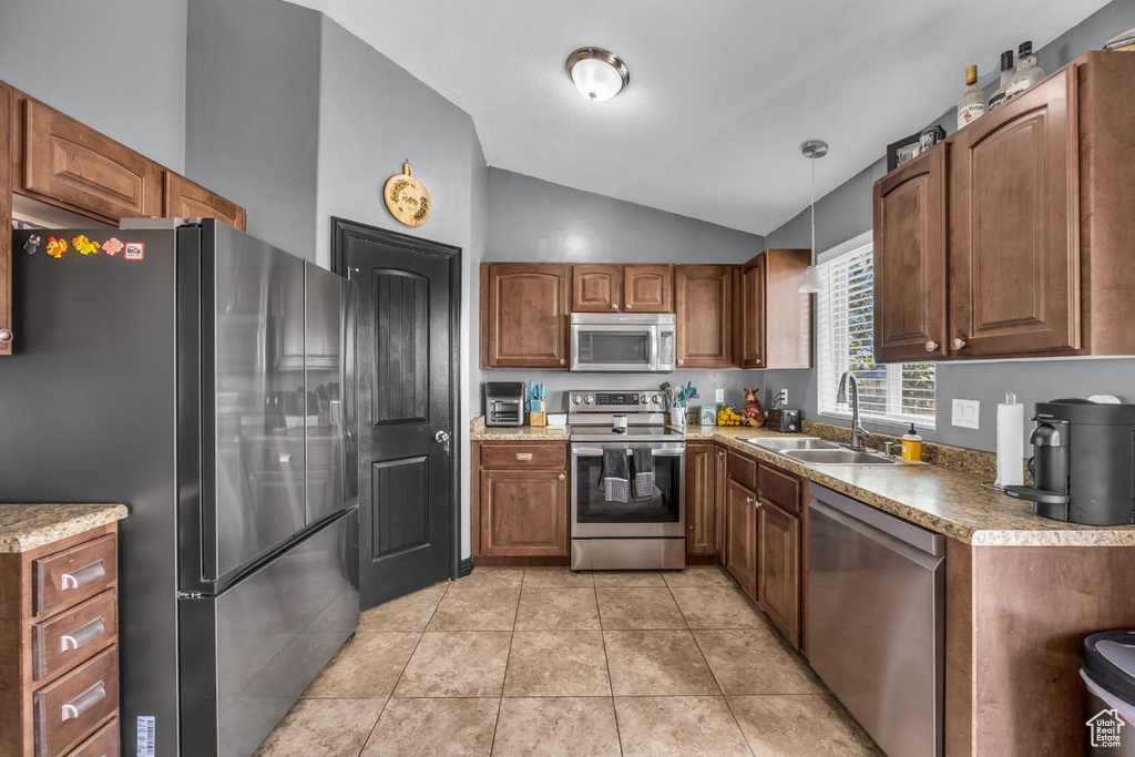 Kitchen with appliances with stainless steel finishes, lofted ceiling, pendant lighting, brown cabinets, and light tile patterned floors