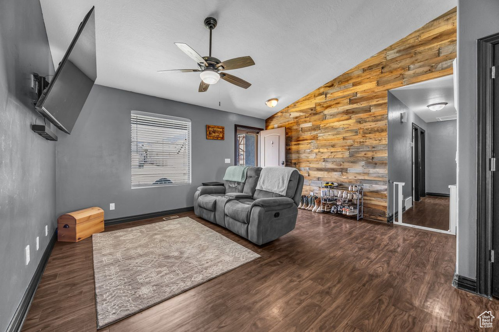 Living area featuring vaulted ceiling, wood finished floors, wood walls, and a ceiling fan