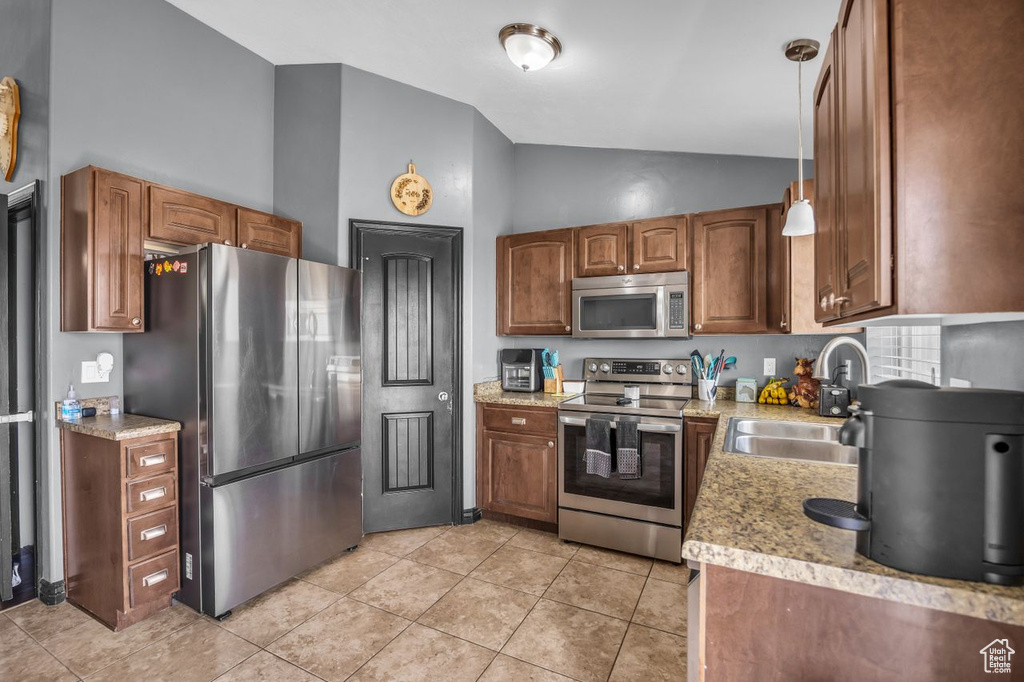 Kitchen with stainless steel appliances, high vaulted ceiling, brown cabinetry, and light tile patterned floors