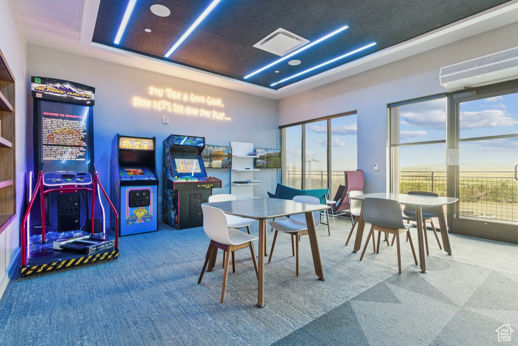Rec room featuring carpet flooring, a tray ceiling, a wall unit AC, and plenty of natural light