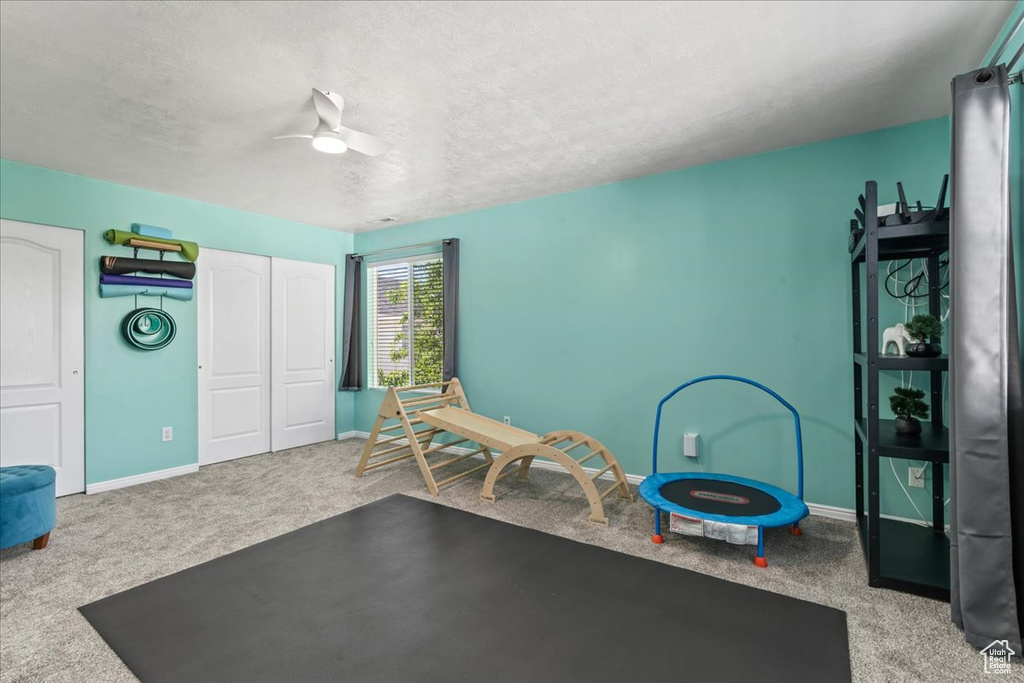 Exercise room featuring carpet flooring, ceiling fan, and a textured ceiling
