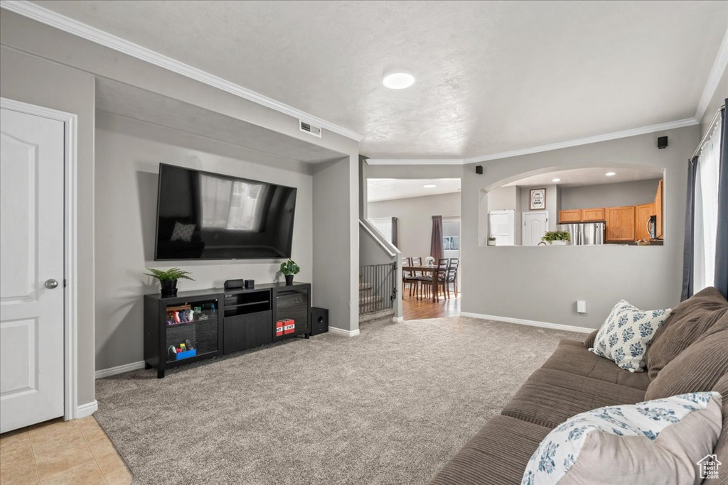 Living room featuring crown molding, arched walkways, recessed lighting, stairway, and light carpet