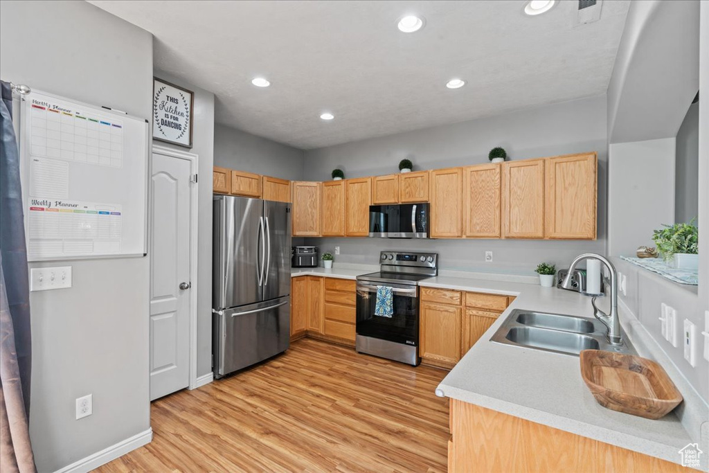 Kitchen with appliances with stainless steel finishes, light wood-style floors, light brown cabinets, recessed lighting, and light countertops