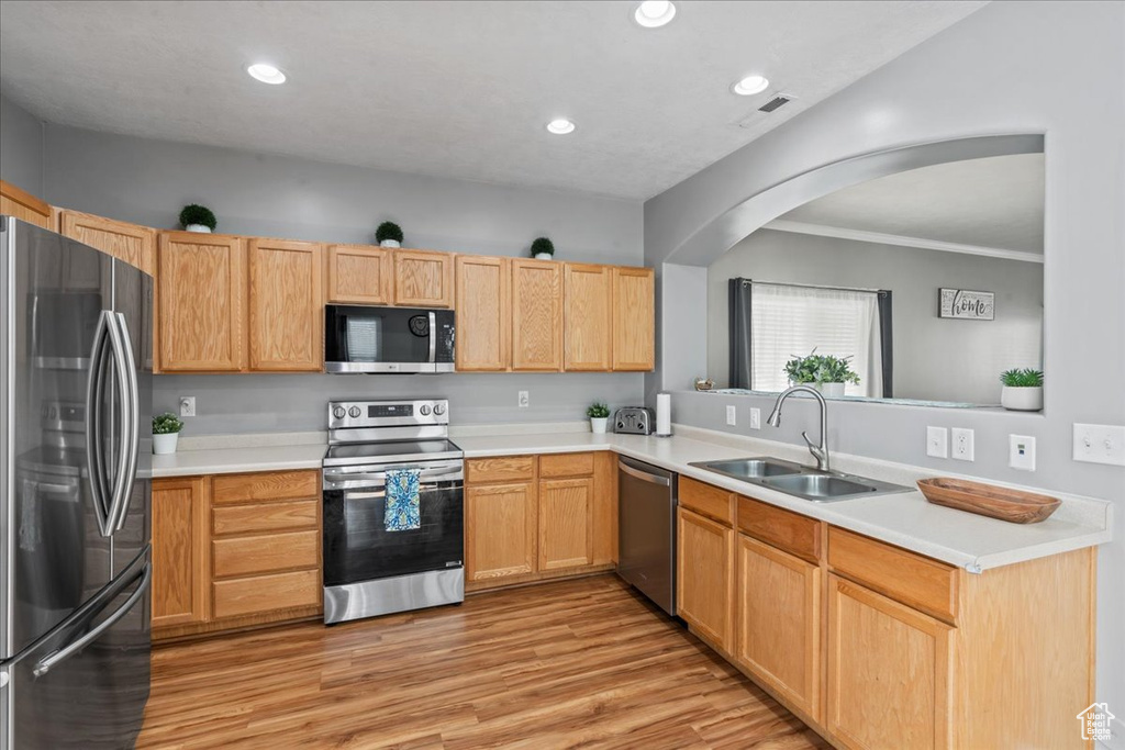 Kitchen with appliances with stainless steel finishes, light wood-type flooring, arched walkways, light countertops, and recessed lighting