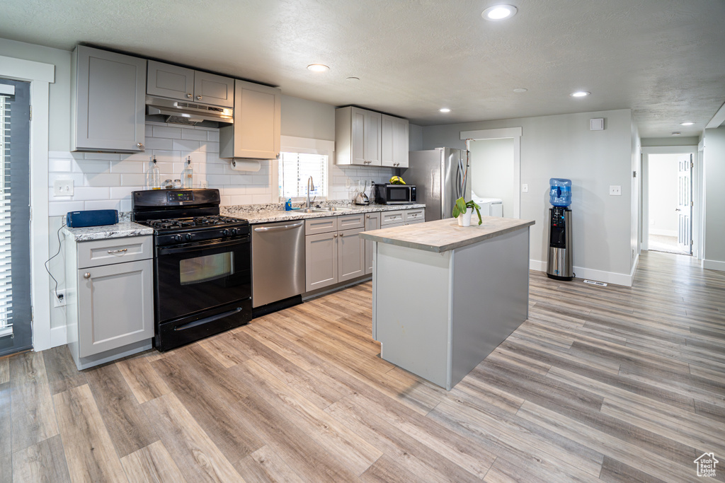 Kitchen with appliances with stainless steel finishes, under cabinet range hood, gray cabinetry, decorative backsplash, and light wood finished floors