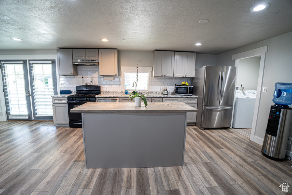 Kitchen featuring stainless steel appliances, washer and clothes dryer, a textured ceiling, decorative backsplash, and a center island