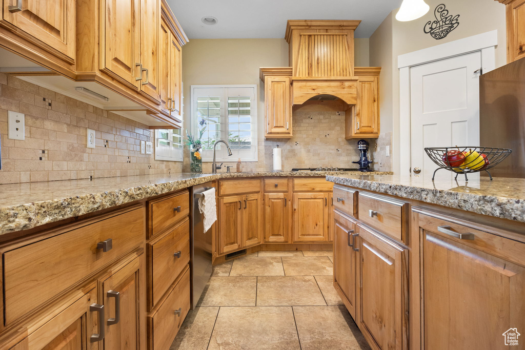Kitchen featuring custom exhaust hood, dishwasher, light stone counters, and decorative backsplash