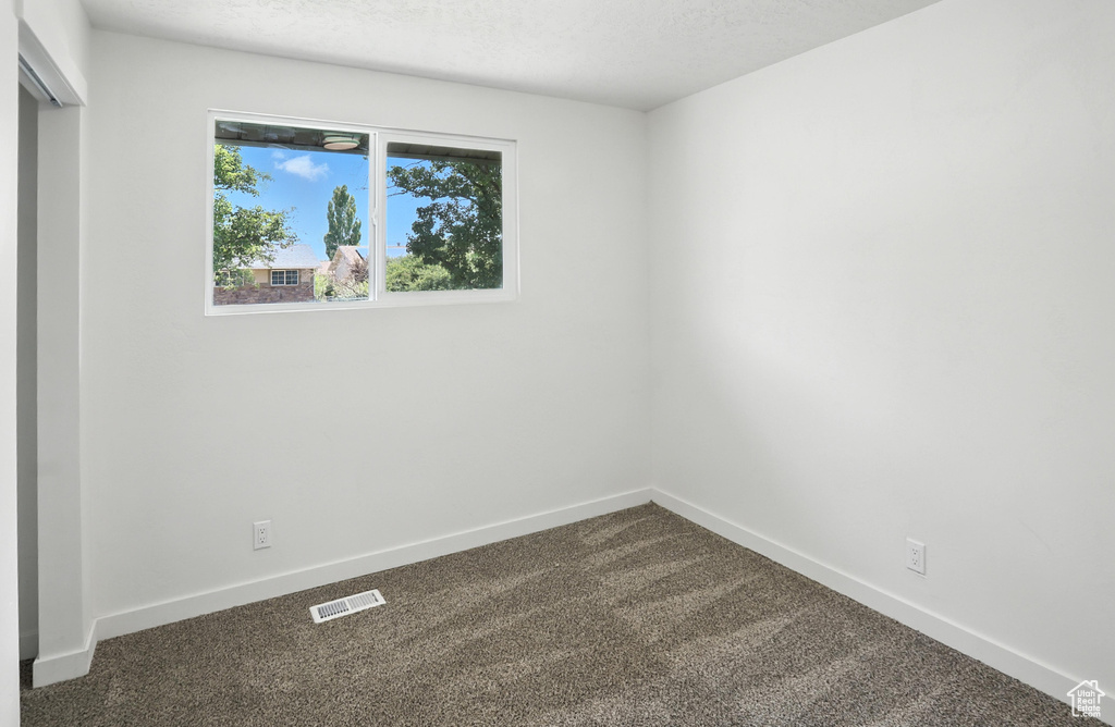 Spare room featuring dark colored carpet and baseboards