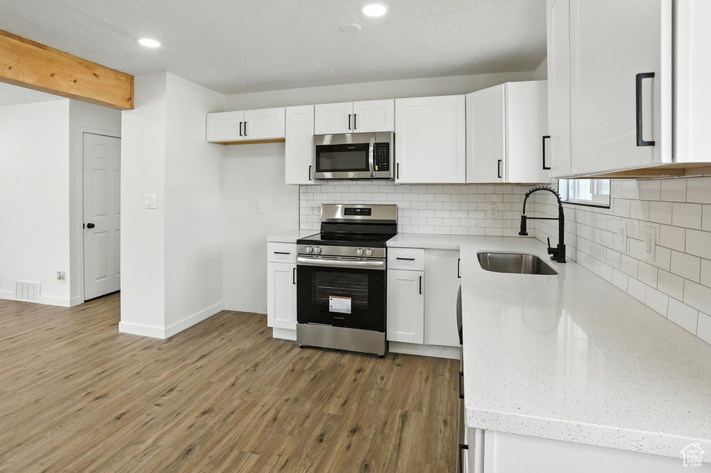 Kitchen with stainless steel appliances, white cabinetry, decorative backsplash, and recessed lighting