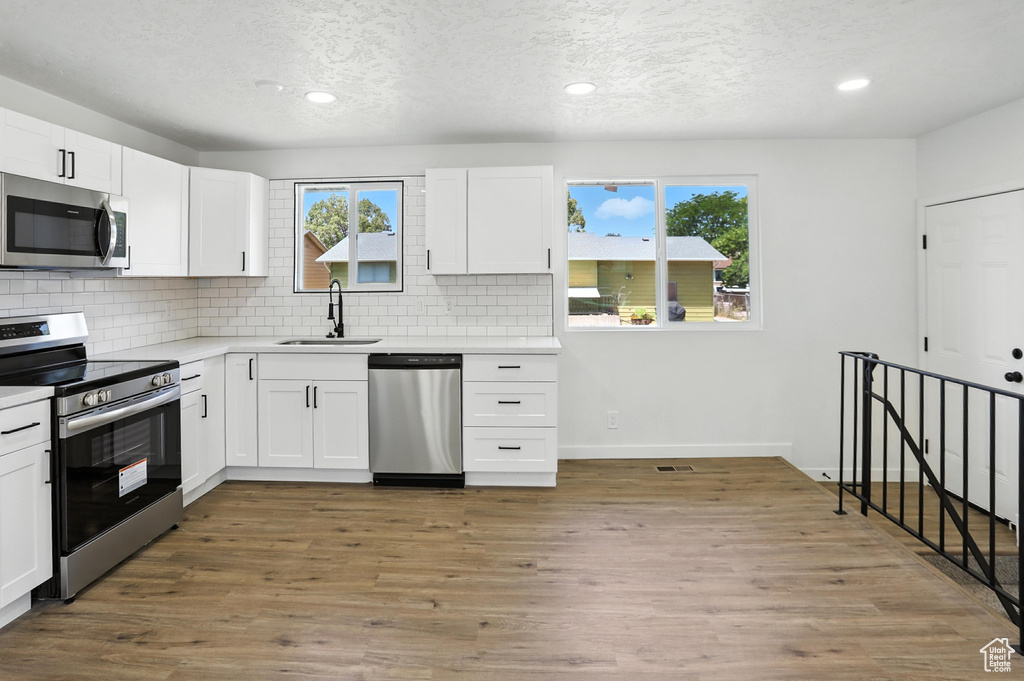 Kitchen with stainless steel appliances, tasteful backsplash, a textured ceiling, white cabinets, and light countertops