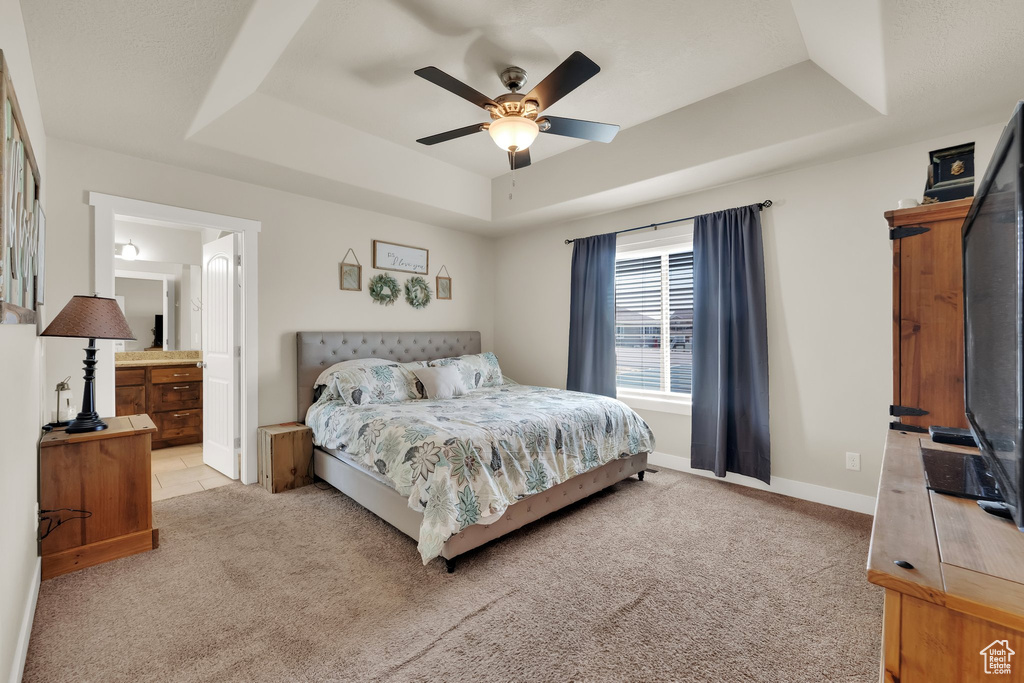 Bedroom featuring a raised ceiling, carpet, ensuite bathroom, and a ceiling fan