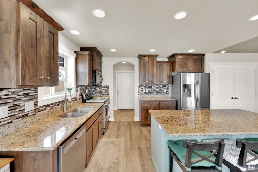 Kitchen featuring appliances with stainless steel finishes, a breakfast bar, light wood-style flooring, decorative backsplash, and light stone counters