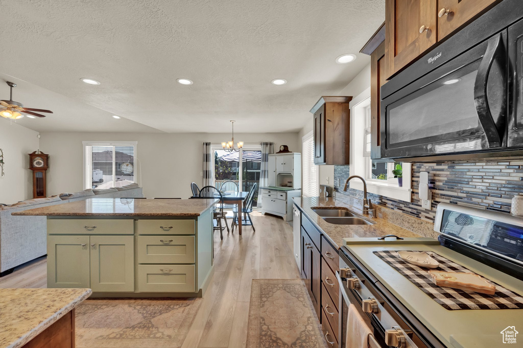Kitchen with black microwave, white range, light wood-style flooring, recessed lighting, and backsplash