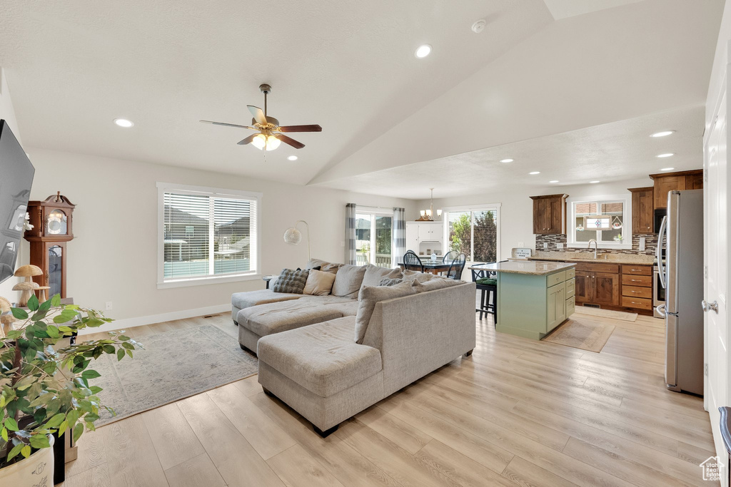 Living room featuring vaulted ceiling, light wood-type flooring, a ceiling fan, recessed lighting, and a chandelier