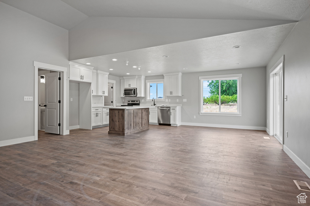 Kitchen with appliances with stainless steel finishes, open floor plan, white cabinets, a center island, and light countertops
