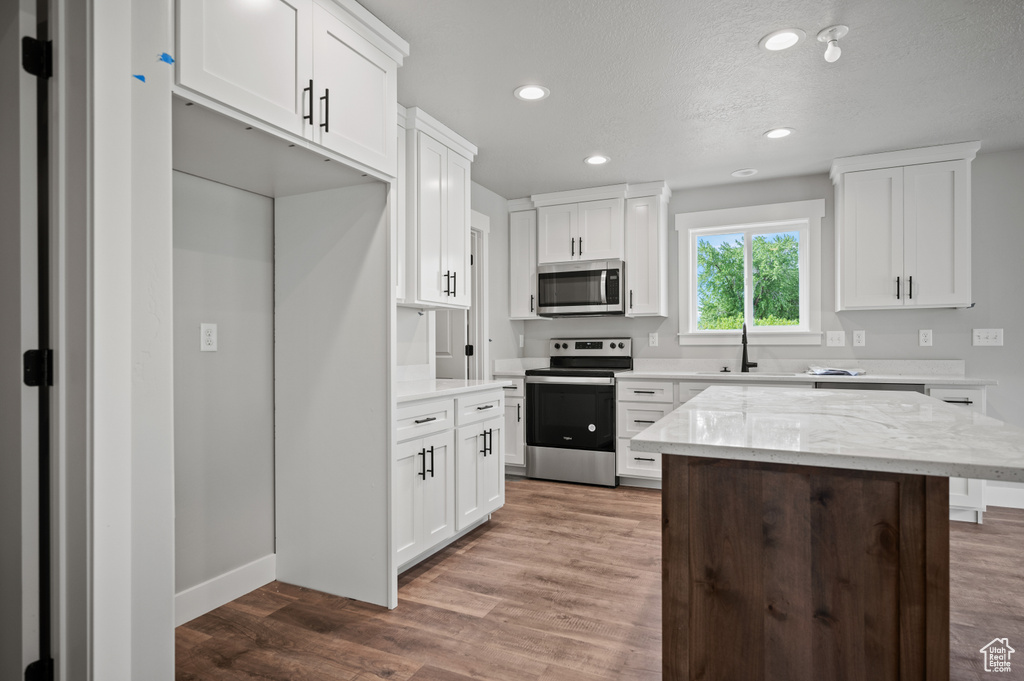 Kitchen featuring appliances with stainless steel finishes, recessed lighting, light wood-style flooring, white cabinets, and light stone counters
