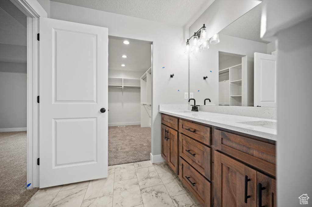 Bathroom featuring double vanity, marble look tile flooring, a spacious closet, and recessed lighting