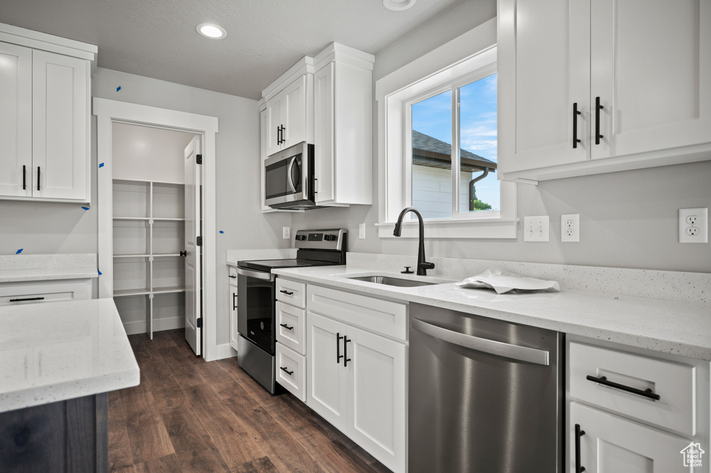 Kitchen with appliances with stainless steel finishes, white cabinetry, dark wood-style floors, light stone countertops, and recessed lighting