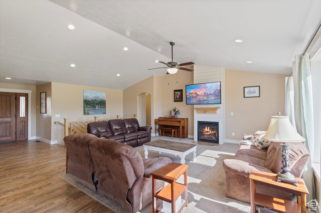 Living room featuring arched walkways, a ceiling fan, light wood-type flooring, lofted ceiling, and a fireplace