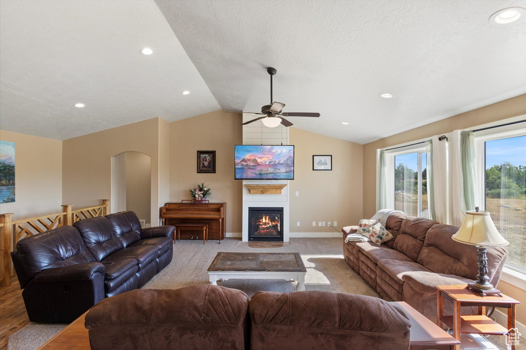 Living room with a ceiling fan, vaulted ceiling, arched walkways, a glass covered fireplace, and recessed lighting