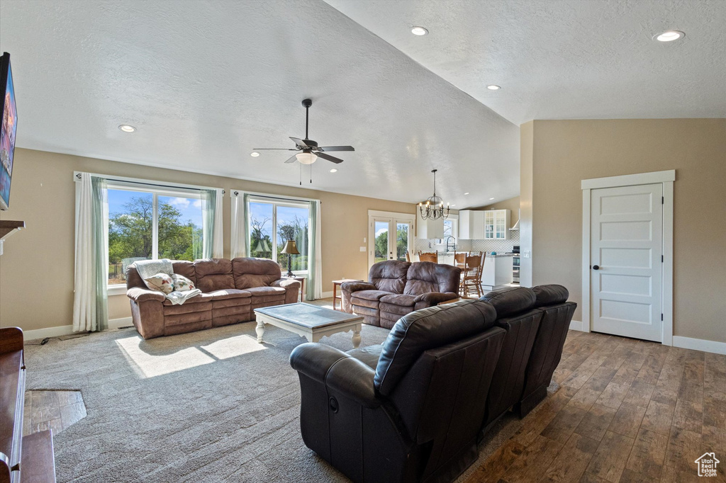 Living area featuring a textured ceiling, a ceiling fan, vaulted ceiling, wood-type flooring, and a chandelier
