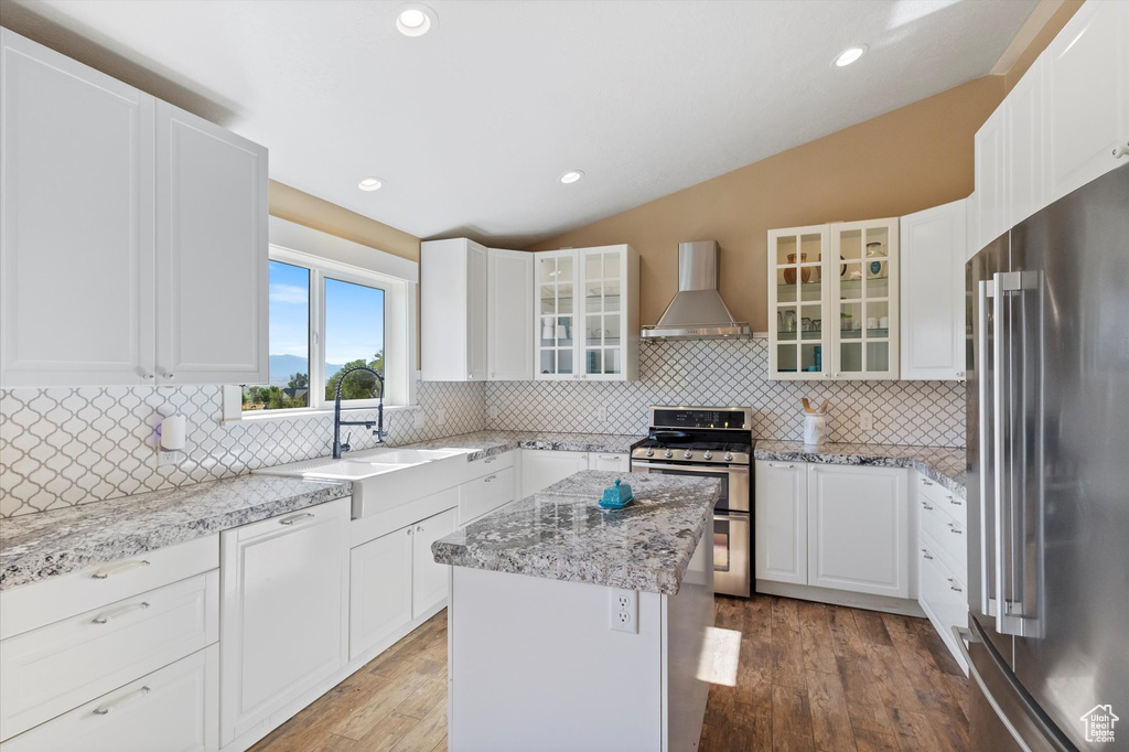 Kitchen with appliances with stainless steel finishes, wall chimney range hood, lofted ceiling, light wood-type flooring, and backsplash