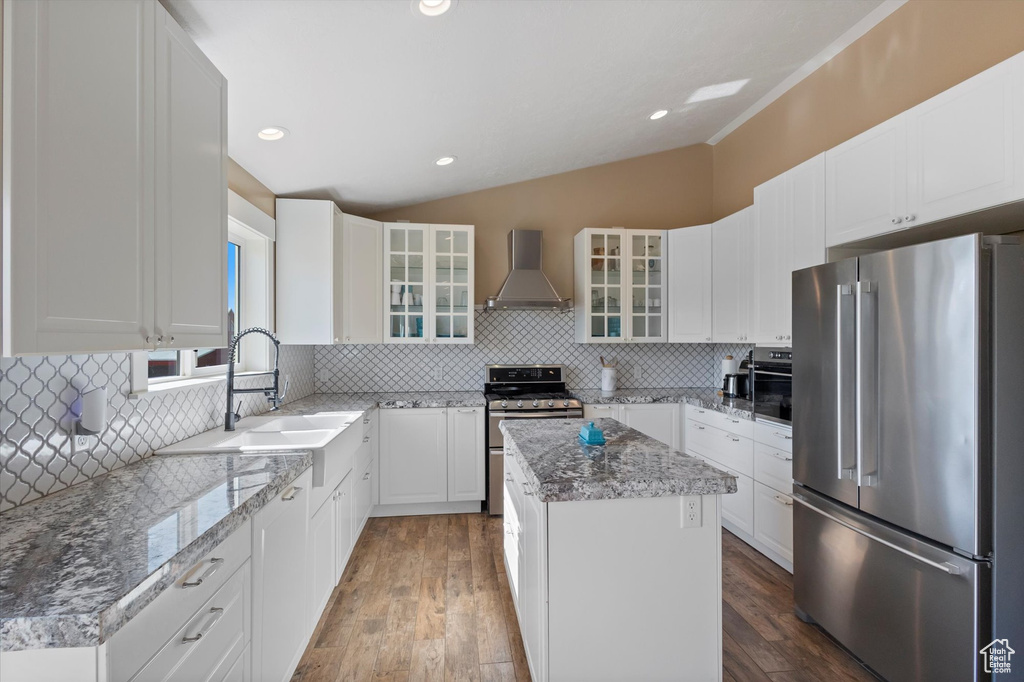 Kitchen featuring stainless steel appliances, wall chimney exhaust hood, lofted ceiling, a kitchen island, and decorative backsplash
