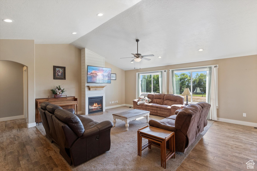 Living room with arched walkways, hardwood / wood-style floors, ceiling fan, a fireplace, and lofted ceiling
