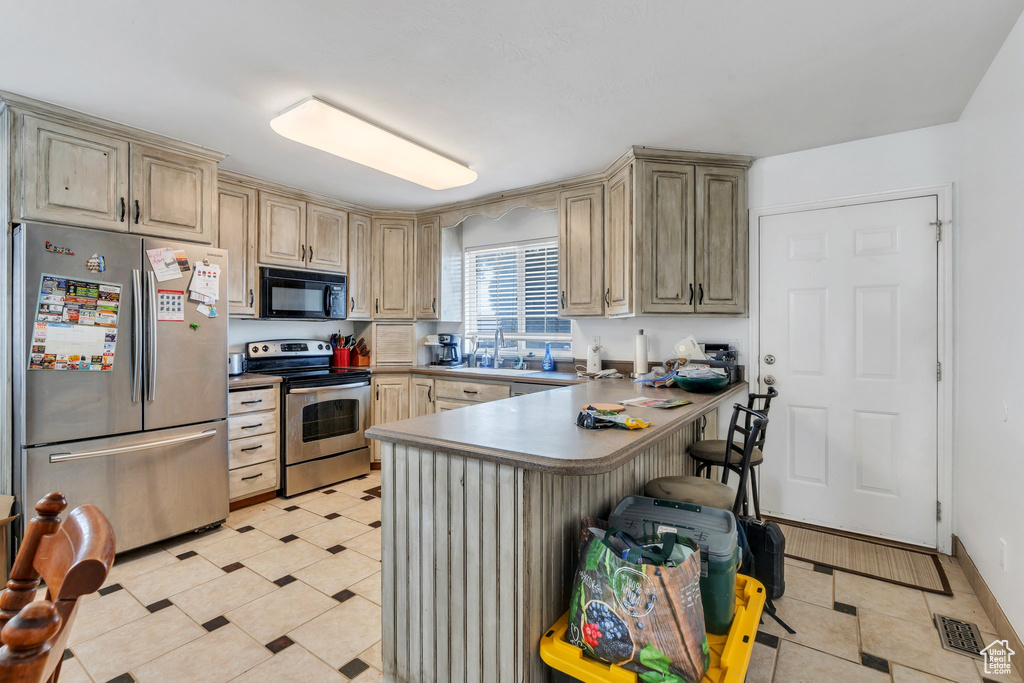 Kitchen with stainless steel appliances, a peninsula, a kitchen bar, cream cabinets, and light tile patterned floors