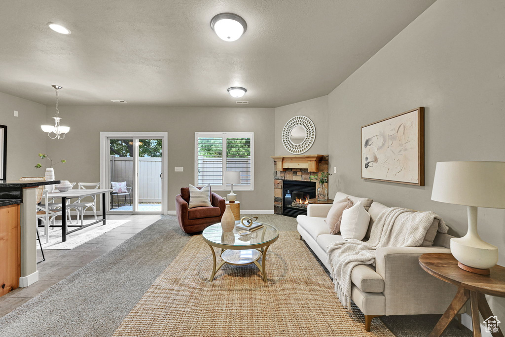 Living area featuring a stone fireplace, light tile patterned floors, a textured ceiling, and a chandelier