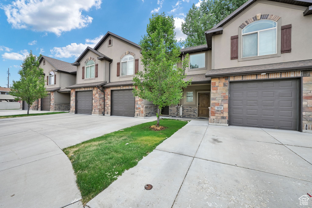 View of front of house featuring an attached garage, driveway, stone siding, and stucco siding