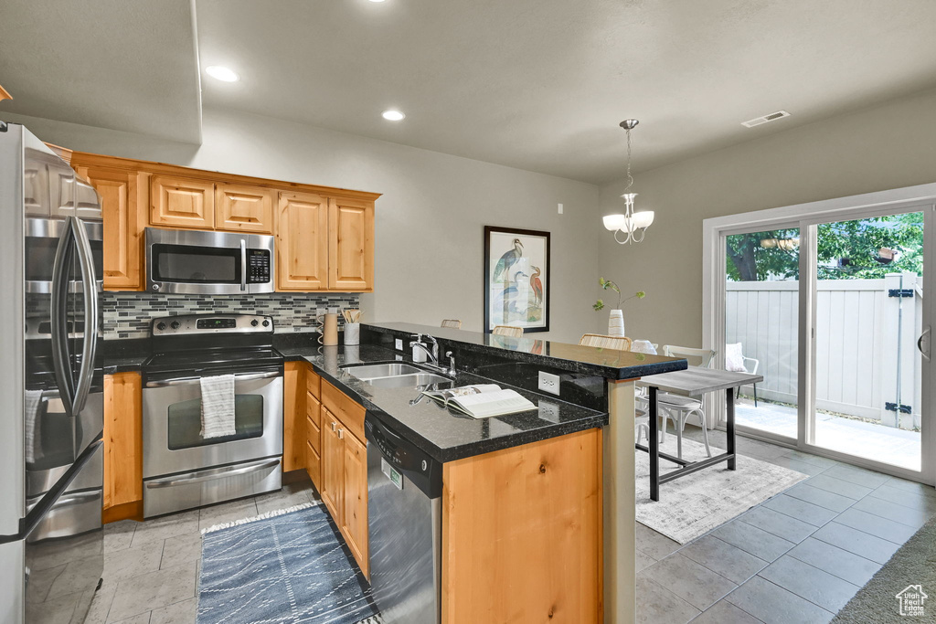 Kitchen with appliances with stainless steel finishes, a peninsula, decorative backsplash, recessed lighting, and a chandelier