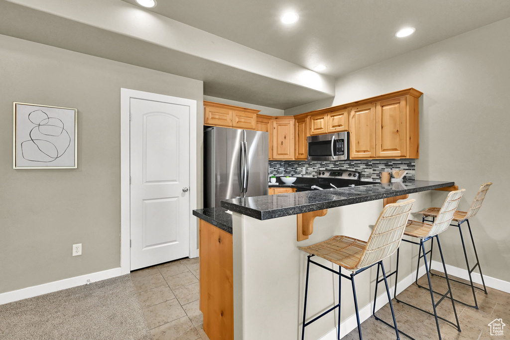 Kitchen with appliances with stainless steel finishes, backsplash, a breakfast bar area, a peninsula, and tile counters