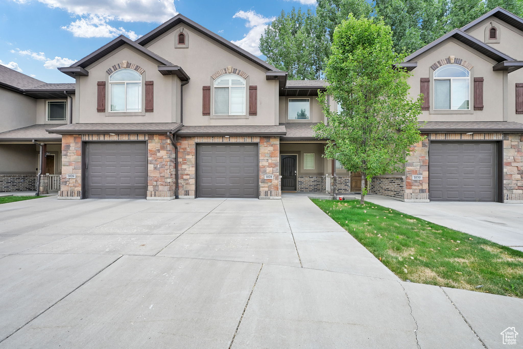 View of property with stucco siding, a garage, driveway, and stone siding