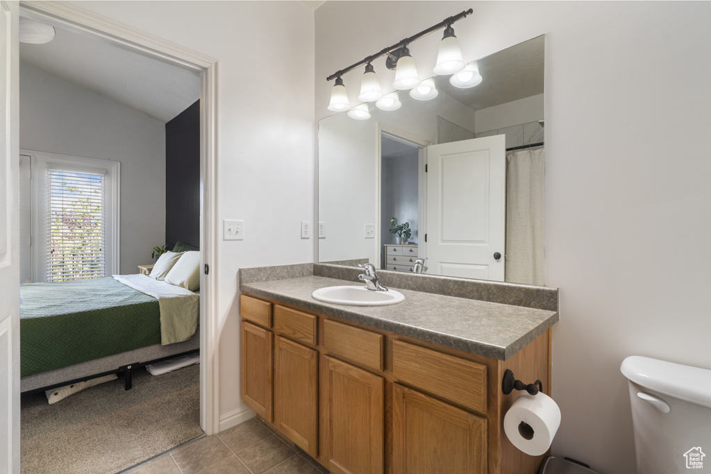 Ensuite bathroom featuring vanity, tile patterned floors, and vaulted ceiling
